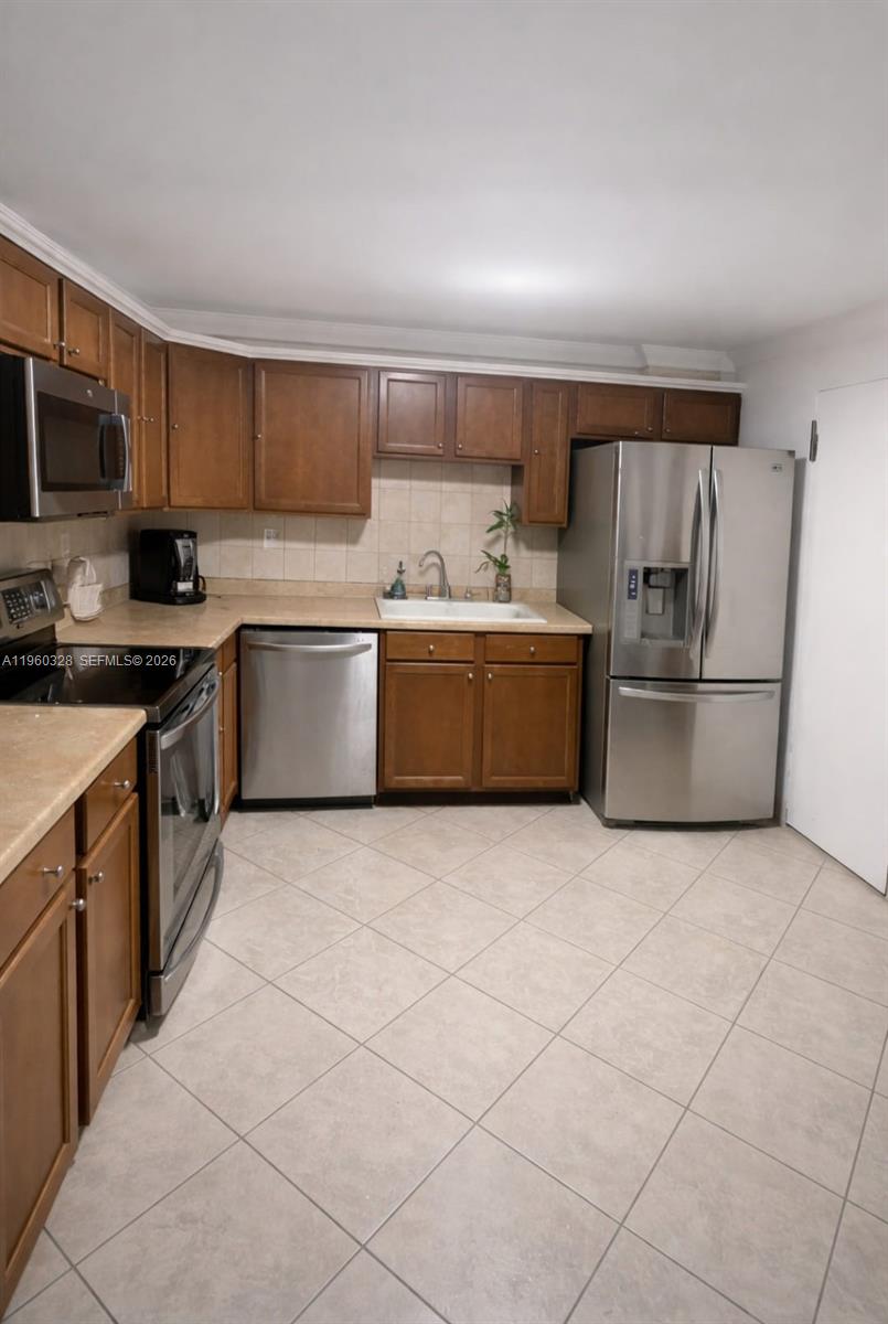 A kitchen features brown wooden cabinets, stainless steel appliances, and light-colored tile flooring — 1470 NE 125th Ter # 701, North Miami FL 33161, NORTH MIAMI, FL