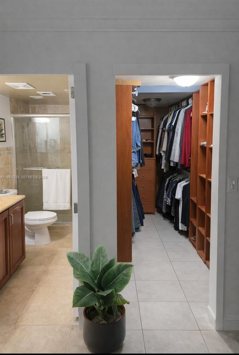 A view of a bathroom and a walk-in closet with wooden shelving and tile flooring — 1470 NE 125th Ter # 701, North Miami FL 33161, NORTH MIAMI, FL