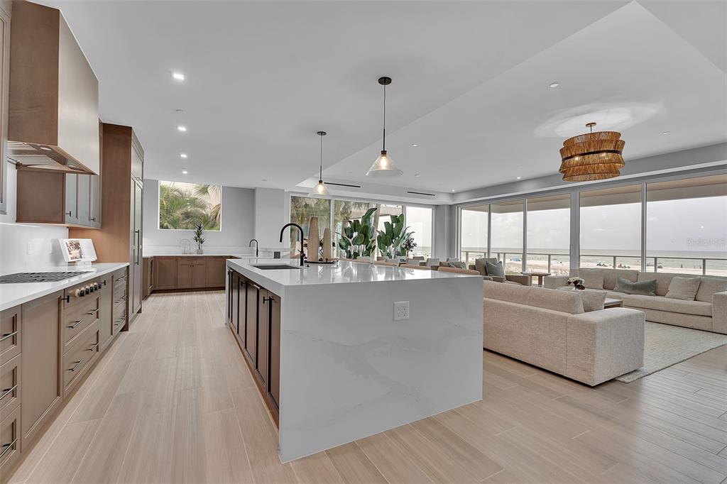 A modern open-concept kitchen and living area features a large marble island and ocean views — 70 AVENIDA VENECCIA UNIT 201, SARASOTA, FL