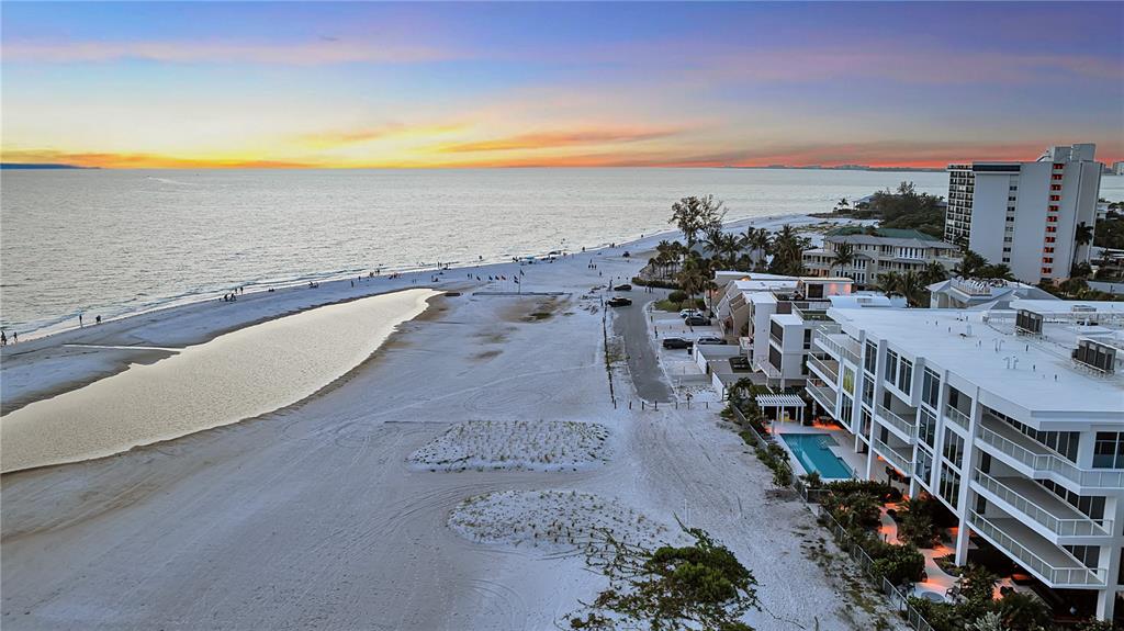 An aerial view shows a white sand beach, a tidal pool, and beachfront residential buildings — 70 AVENIDA VENECCIA UNIT 201, SARASOTA, FL
