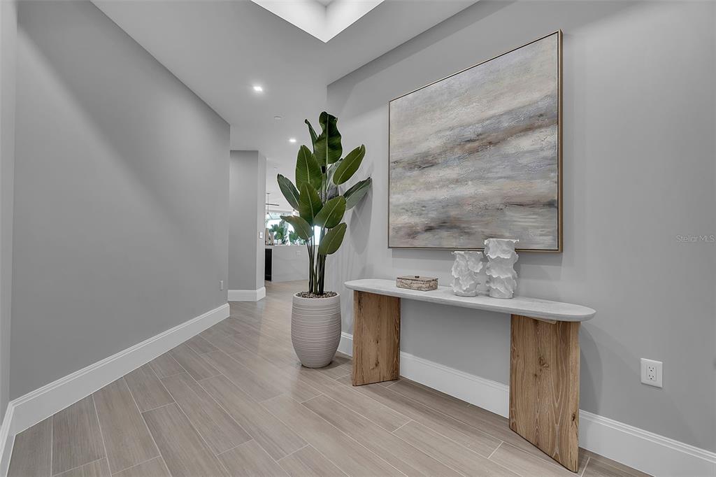 A modern entryway features light wood-look tile flooring, a console table, and a potted plant — 70 AVENIDA VENECCIA UNIT 201, SARASOTA, FL