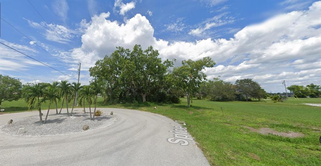 A paved cul-de-sac features a small landscaped island with palm trees and surrounding grassy lots — 17172 SPICE LANE, PUNTA GORDA, FL
