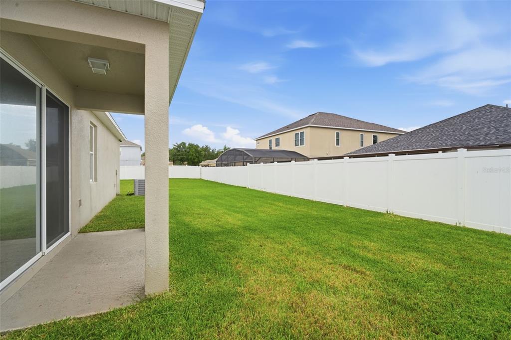 A view of a grassy backyard with a covered patio and a white vinyl fence — 231 DOE RUN DRIVE, WINTER GARDEN, FL