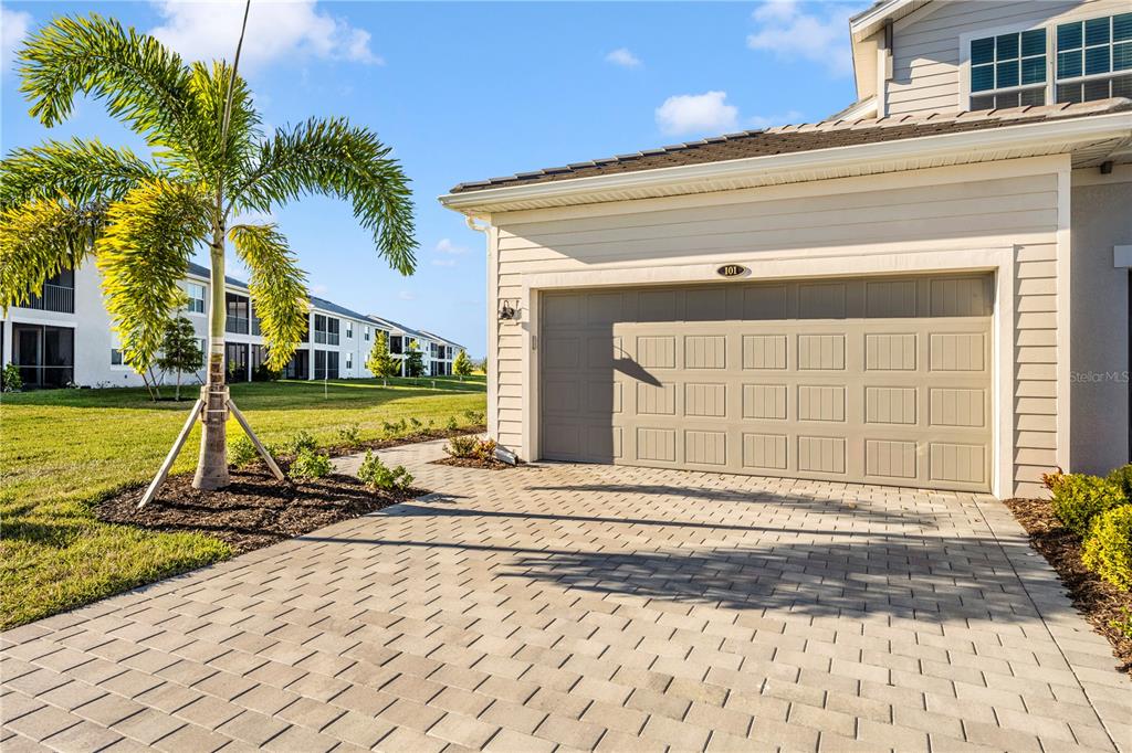 A paved driveway leads to a beige garage door on the side of a house — 17715 BORACAY COURT UNIT 101, VENICE, FL
