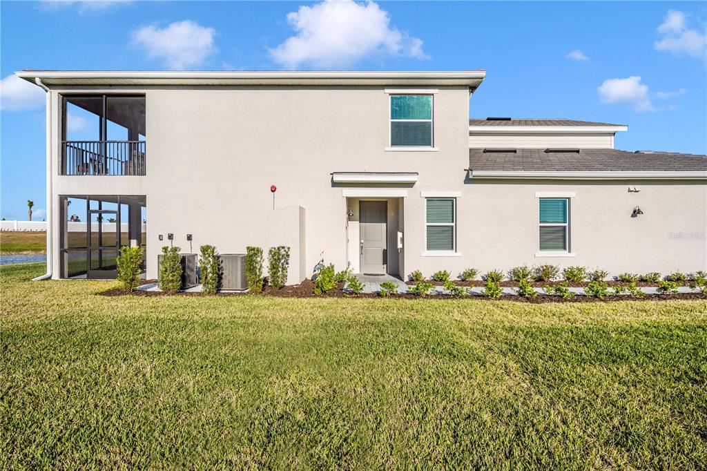 The rear exterior of a two-story house features a screened balcony, patio, and landscaped yard — 17715 BORACAY COURT UNIT 101, VENICE, FL