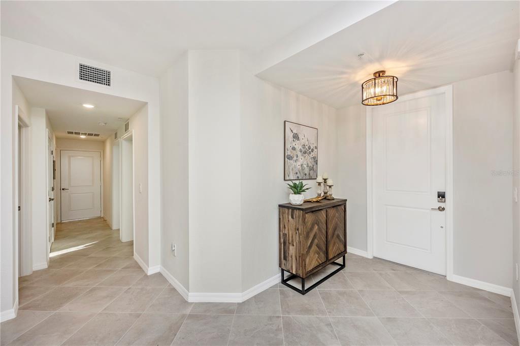 A bright entryway features light tile flooring, a wooden cabinet, and a modern ceiling light — 17715 BORACAY COURT UNIT 101, VENICE, FL