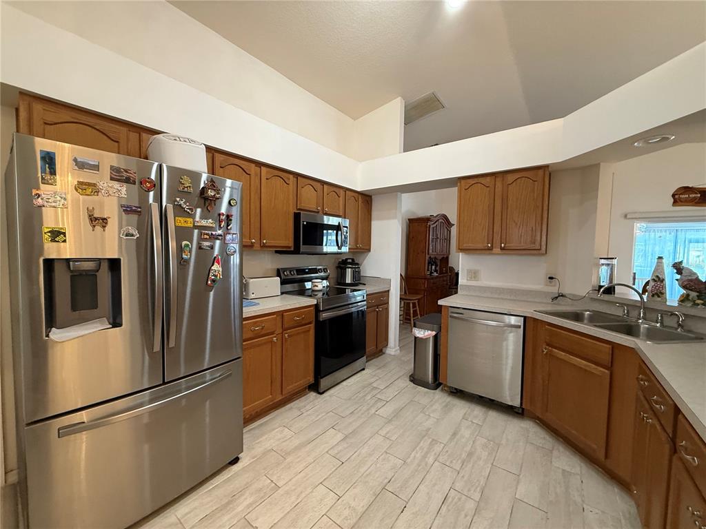 A kitchen features wood cabinets, stainless steel appliances, and light-colored tile flooring — 25607 BELLE HELENE, LEESBURG, FL