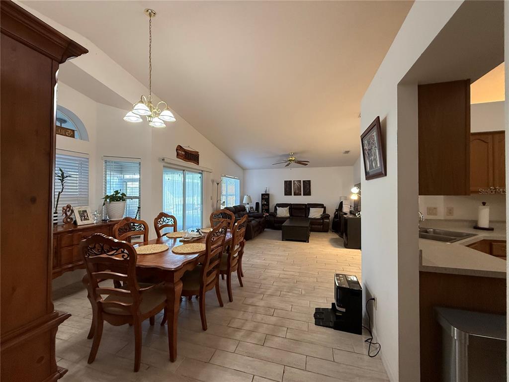 An open-concept dining area and living room with tile flooring and vaulted ceilings — 25607 BELLE HELENE, LEESBURG, FL