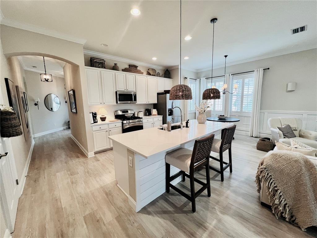 A kitchen features white cabinets, a central island with bar seating, and light wood flooring — 210 LATITUDE PLACE, APOLLO BEACH, FL