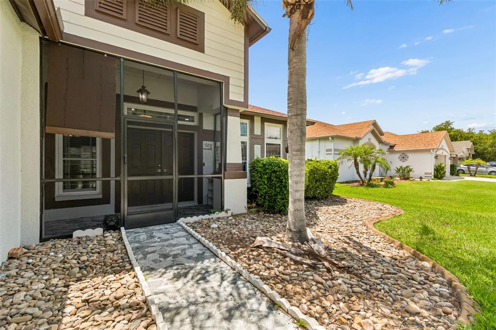 A stone walkway leads to a screened-in front entryway of a house with tan siding — 5737 WYNSTONE LANE, ZEPHYRHILLS, FL
