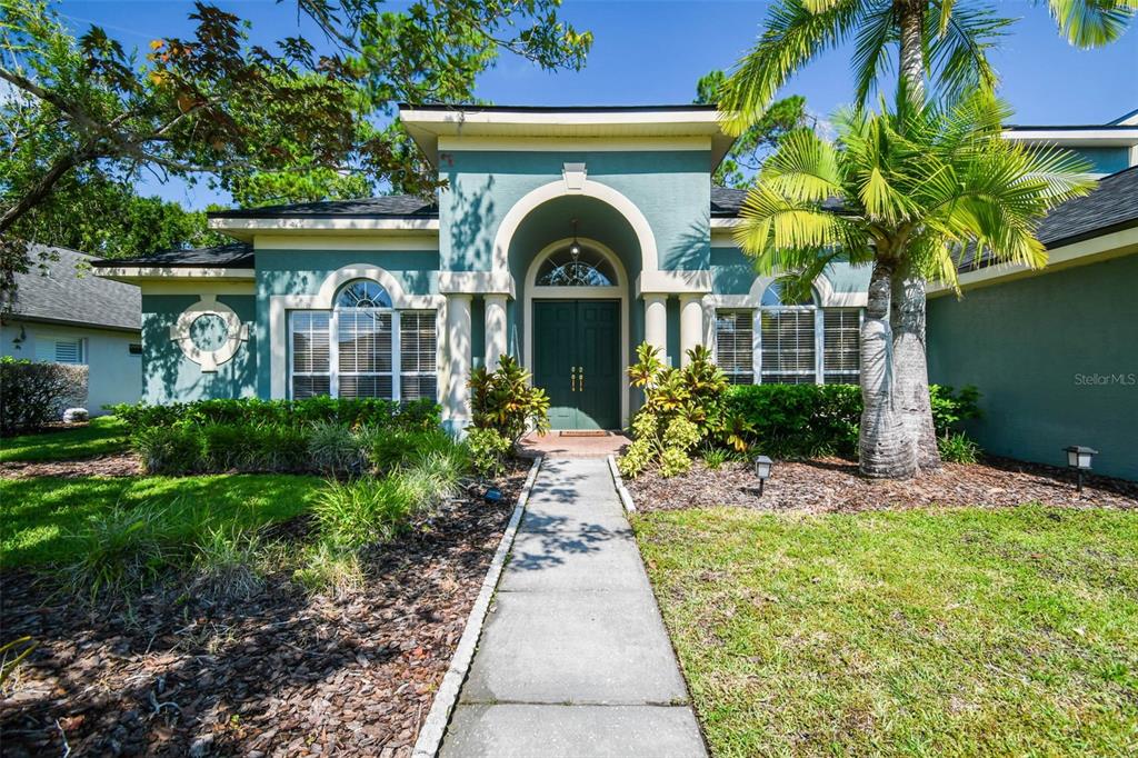 A teal-colored house with a central arched entryway, double doors, and a palm tree — 10526 GREENCREST DRIVE, TAMPA, FL