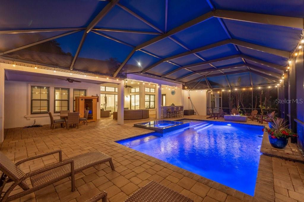 A covered pool patio features a swimming pool, hot tub, and outdoor seating area at night — 5201 ALAFIA FALLS DRIVE, LITHIA, FL