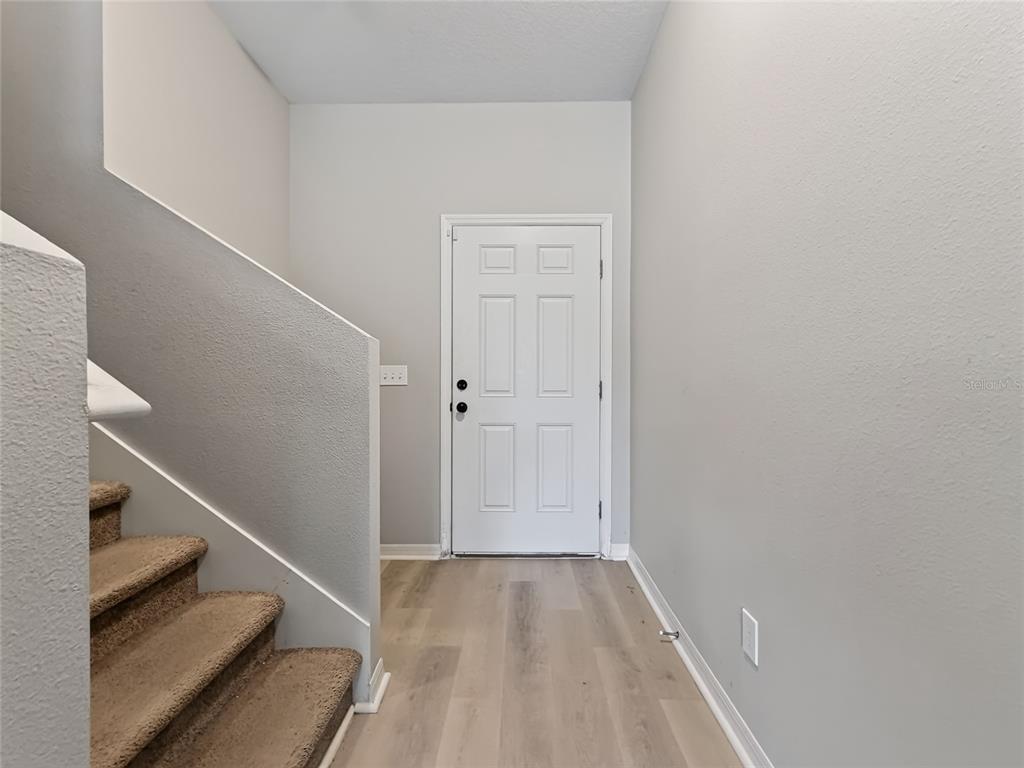An entryway features light wood-look flooring, a white front door, and carpeted stairs — 2610 FLICKER COVE, SANFORD, FL