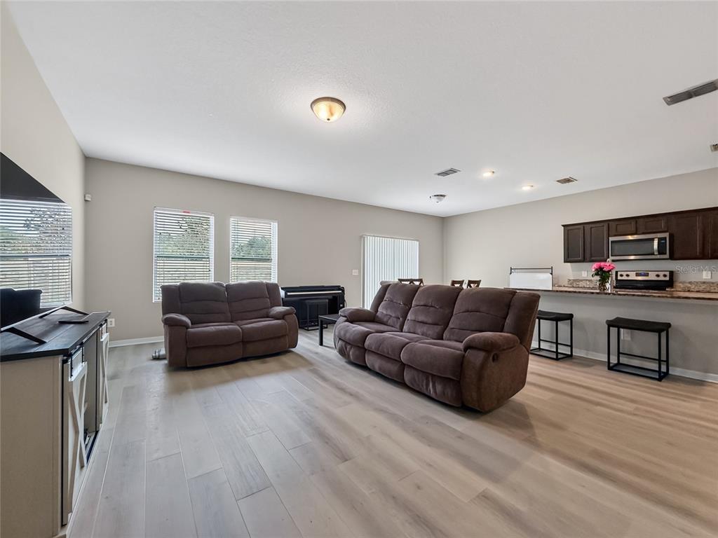 An open-concept living room and kitchen featuring brown reclining sofas and light wood-look flooring — 2610 FLICKER COVE, SANFORD, FL