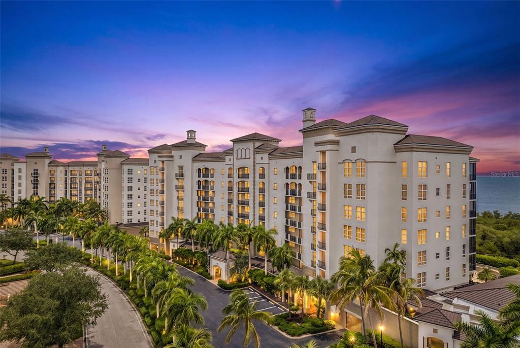 An exterior view of a large, multi-story apartment building surrounded by palm trees at sunset — 3329 SUNSET KEY CIRCLE UNIT 204, PUNTA GORDA, FL