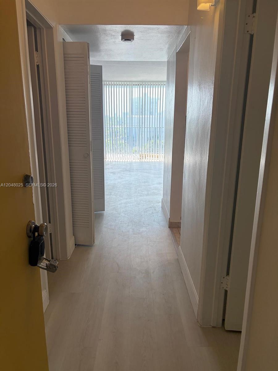 A hallway with light-colored flooring leads toward a room with floor-to-ceiling vertical blinds — 12590 NE 16th Ave # 512, North Miami FL 33161, NORTH MIAMI, FL