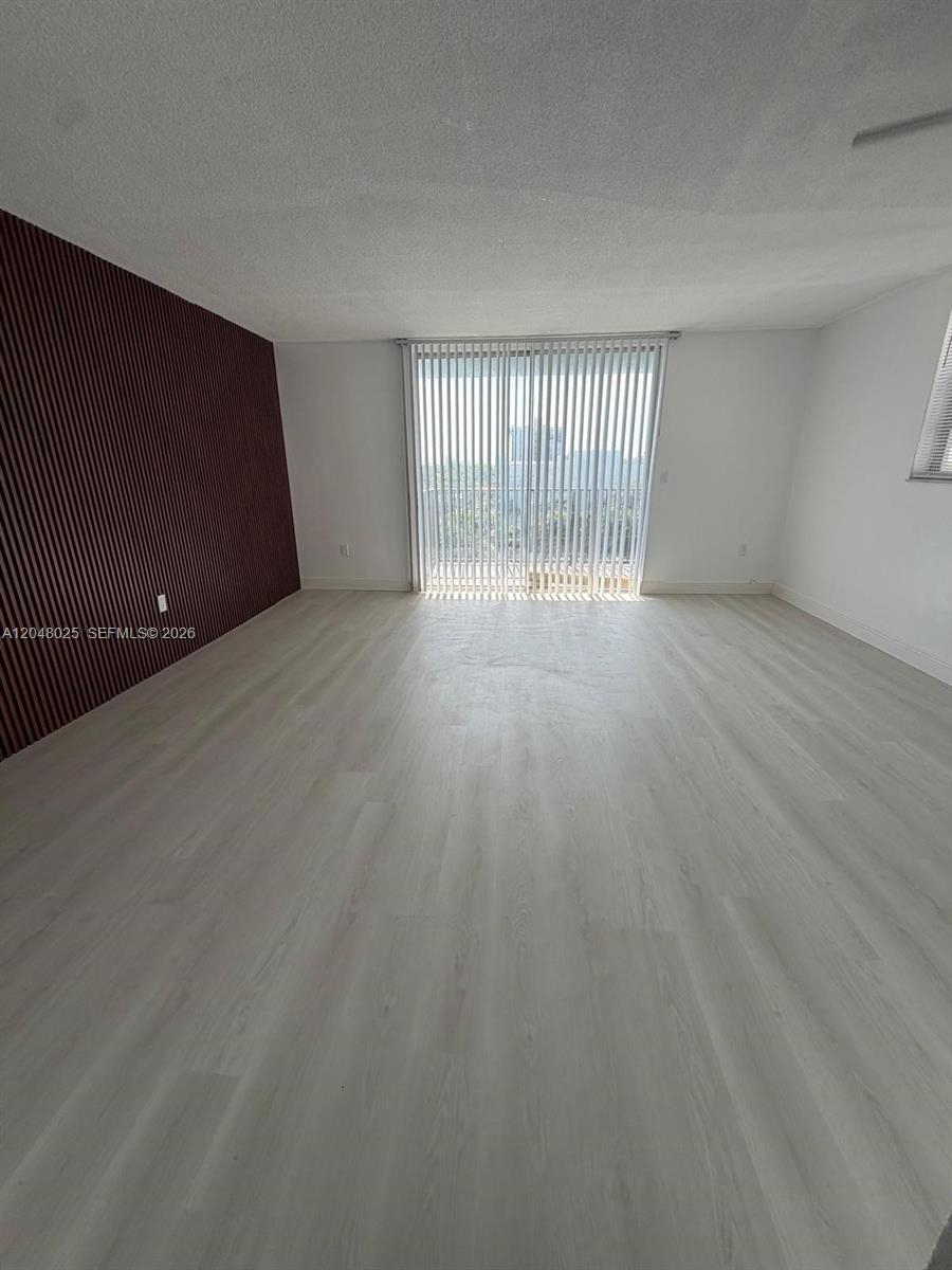 An empty room features light wood-look flooring, white walls, and a dark vertical-slatted accent wall — 12590 NE 16th Ave # 512, North Miami FL 33161, NORTH MIAMI, FL