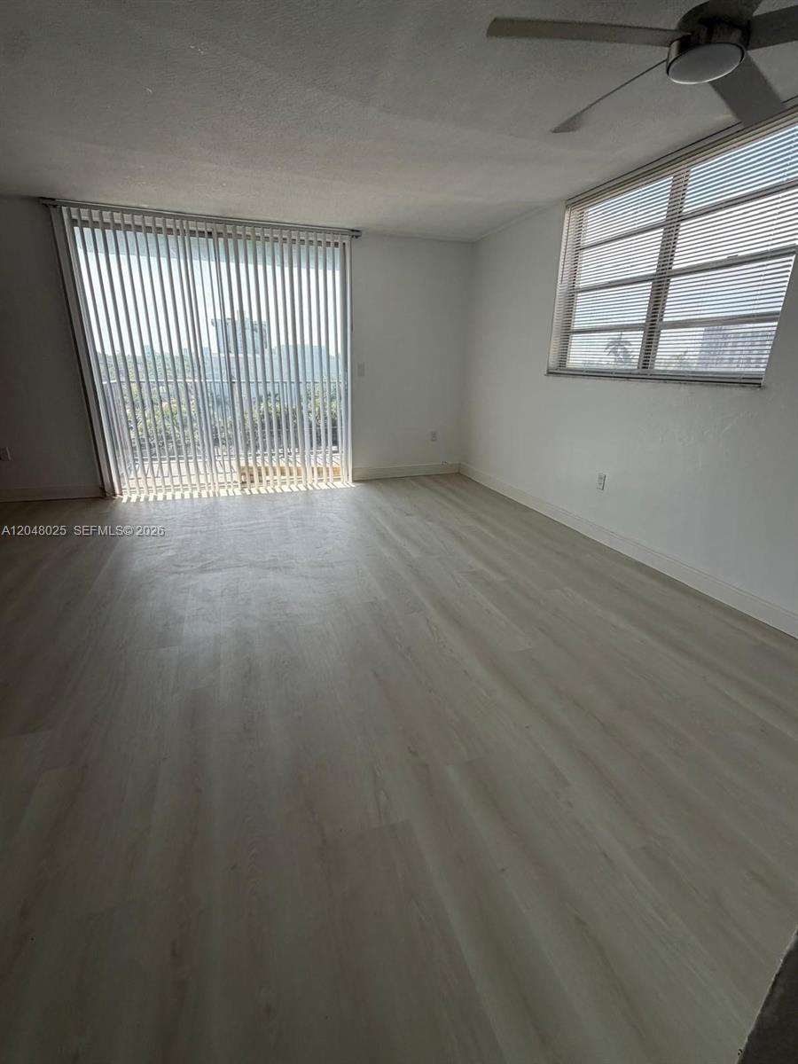 An empty room features light-colored wood-look flooring, white walls, vertical blinds, and a ceiling fan — 12590 NE 16th Ave # 512, North Miami FL 33161, NORTH MIAMI, FL