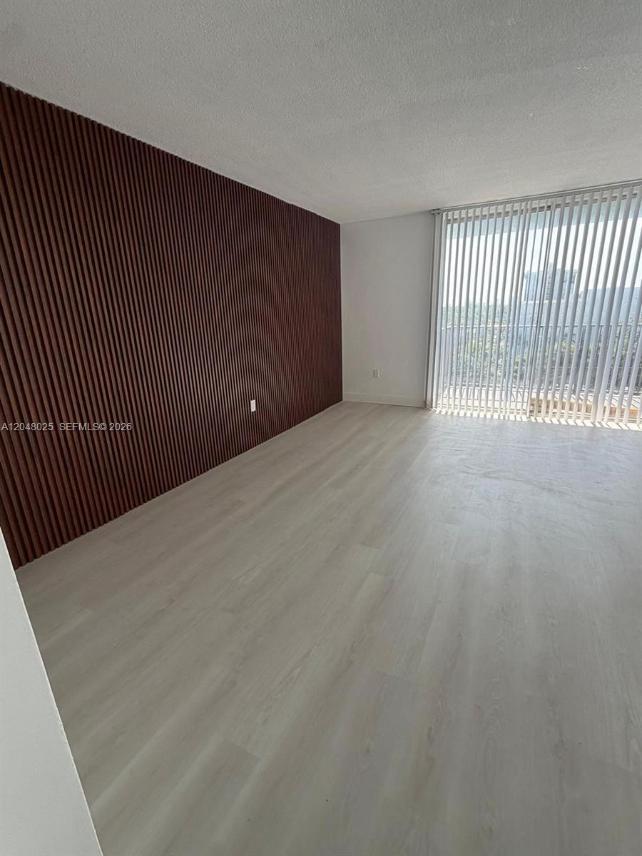 An empty room features light wood-look flooring and a dark wood slat accent wall — 12590 NE 16th Ave # 512, North Miami FL 33161, NORTH MIAMI, FL