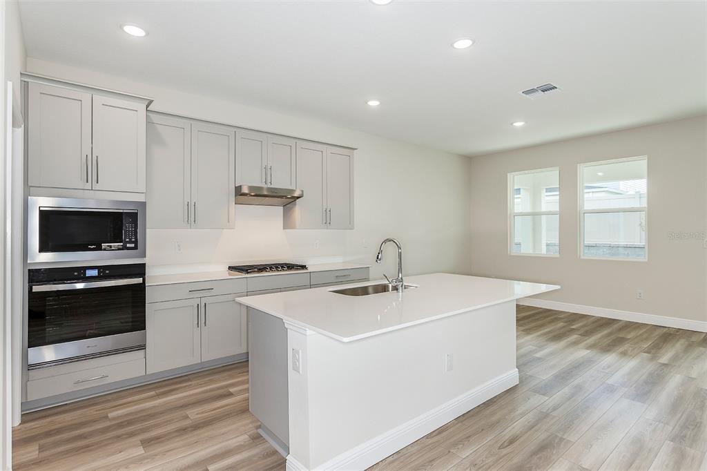 A modern kitchen features light gray cabinets, white countertops, a center island, and stainless appliances — 33437 TWILIGHT SEA PLACE, DADE CITY, FL