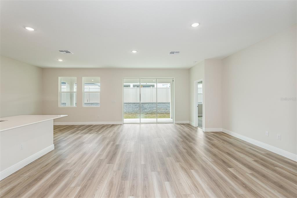 An open-concept living area features light wood-look flooring, recessed lighting, and sliding glass patio doors — 33437 TWILIGHT SEA PLACE, DADE CITY, FL