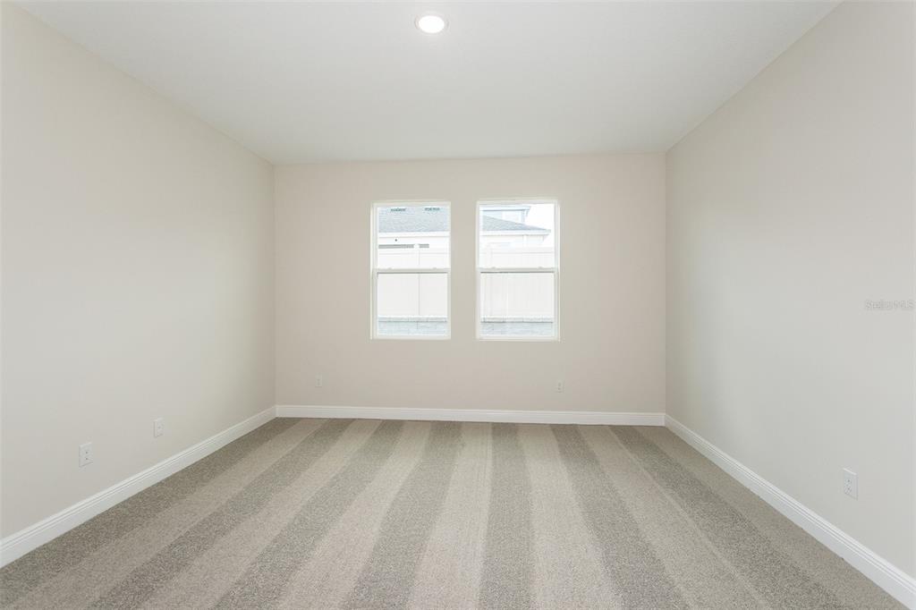 An empty bedroom features beige walls, white trim, and gray striped carpeting — 33437 TWILIGHT SEA PLACE, DADE CITY, FL
