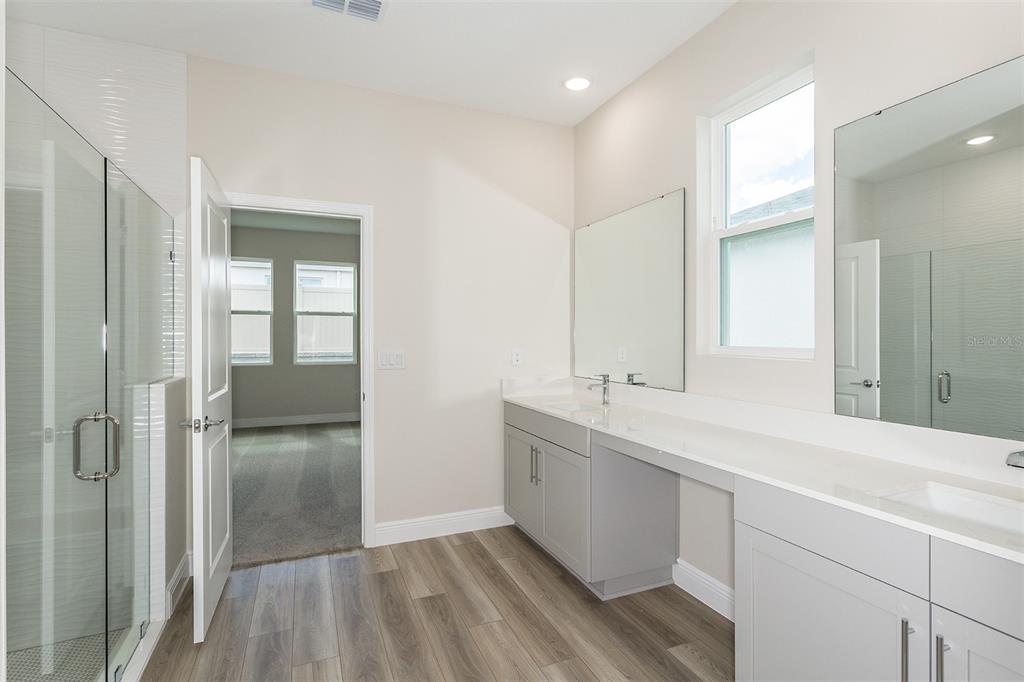 A modern bathroom features a double vanity with grey cabinets, white countertops, and a glass shower — 33437 TWILIGHT SEA PLACE, DADE CITY, FL