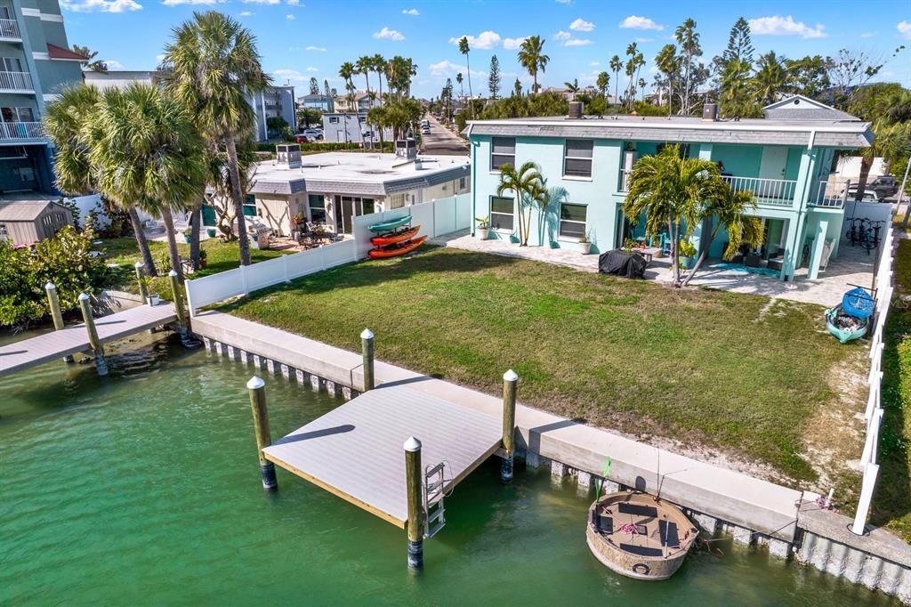An aerial view of a waterfront property featuring a dock, lawn, and two-story teal building — 117 140TH AVENUE E UNIT A, MADEIRA BEACH, FL