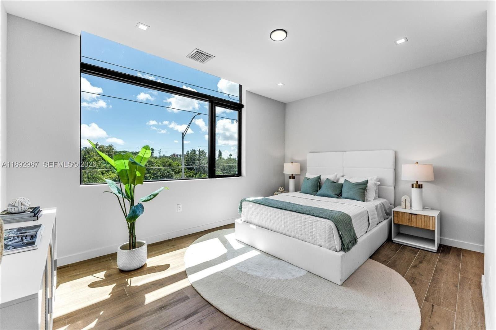 A modern bedroom features a large window, white walls, wood floors, and a queen bed — 527 NE 61st St, Miami FL 33137, MIAMI, FL