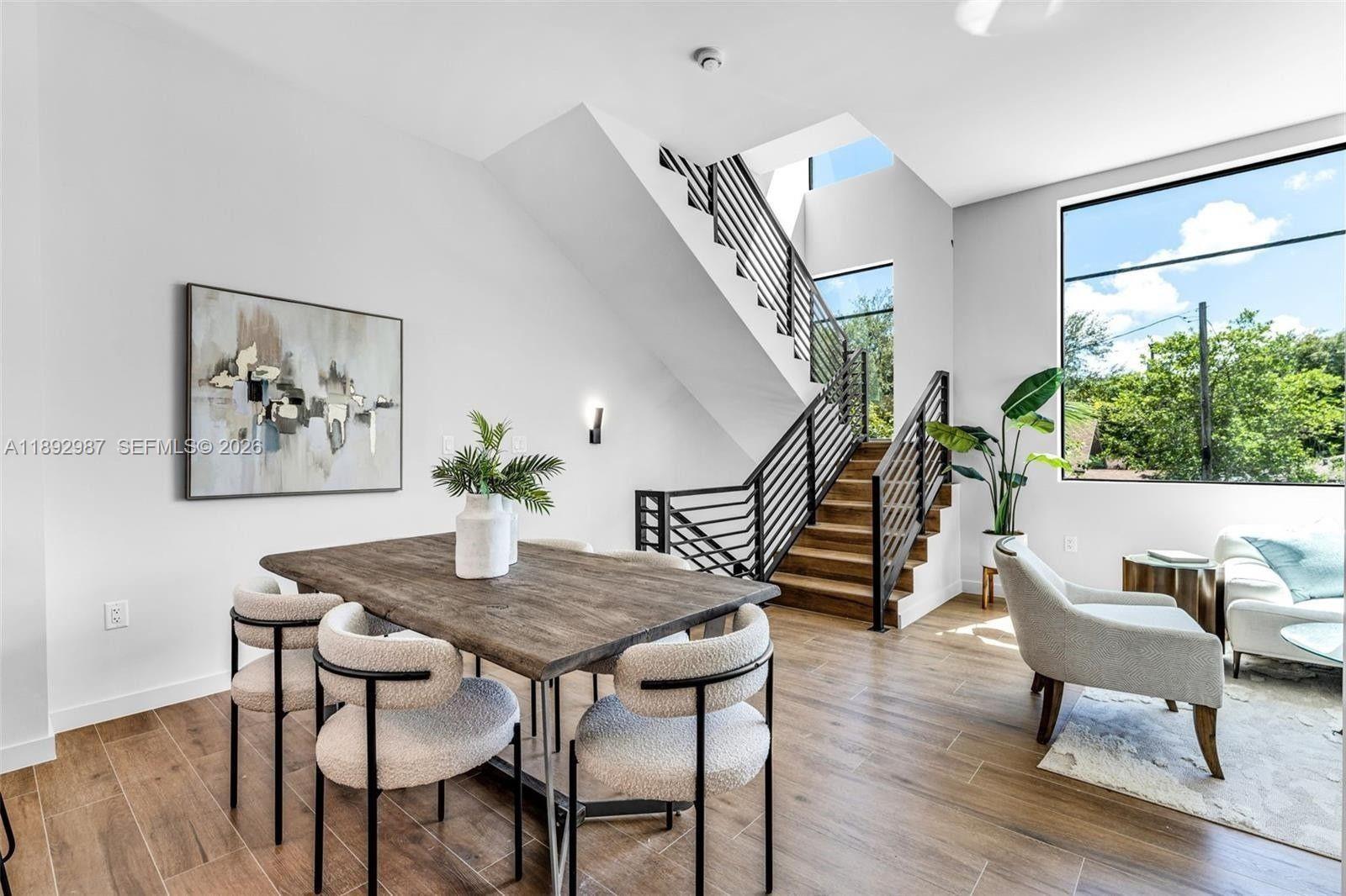 A dining area features a wooden table, modern chairs, and a staircase with metal railings — 527 NE 61st St, Miami FL 33137, MIAMI, FL