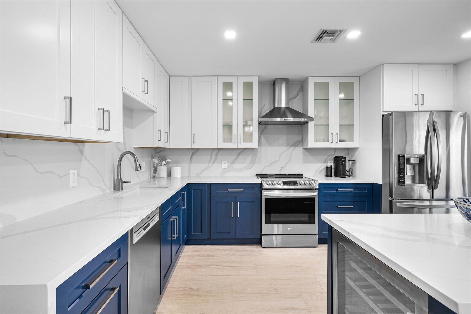 A kitchen features white upper cabinets, blue lower cabinets, stainless steel appliances, and quartz countertops — 3676 Quail Ridge Drive N, Boynton Beach FL 33436, BOYNTON BEACH, FL