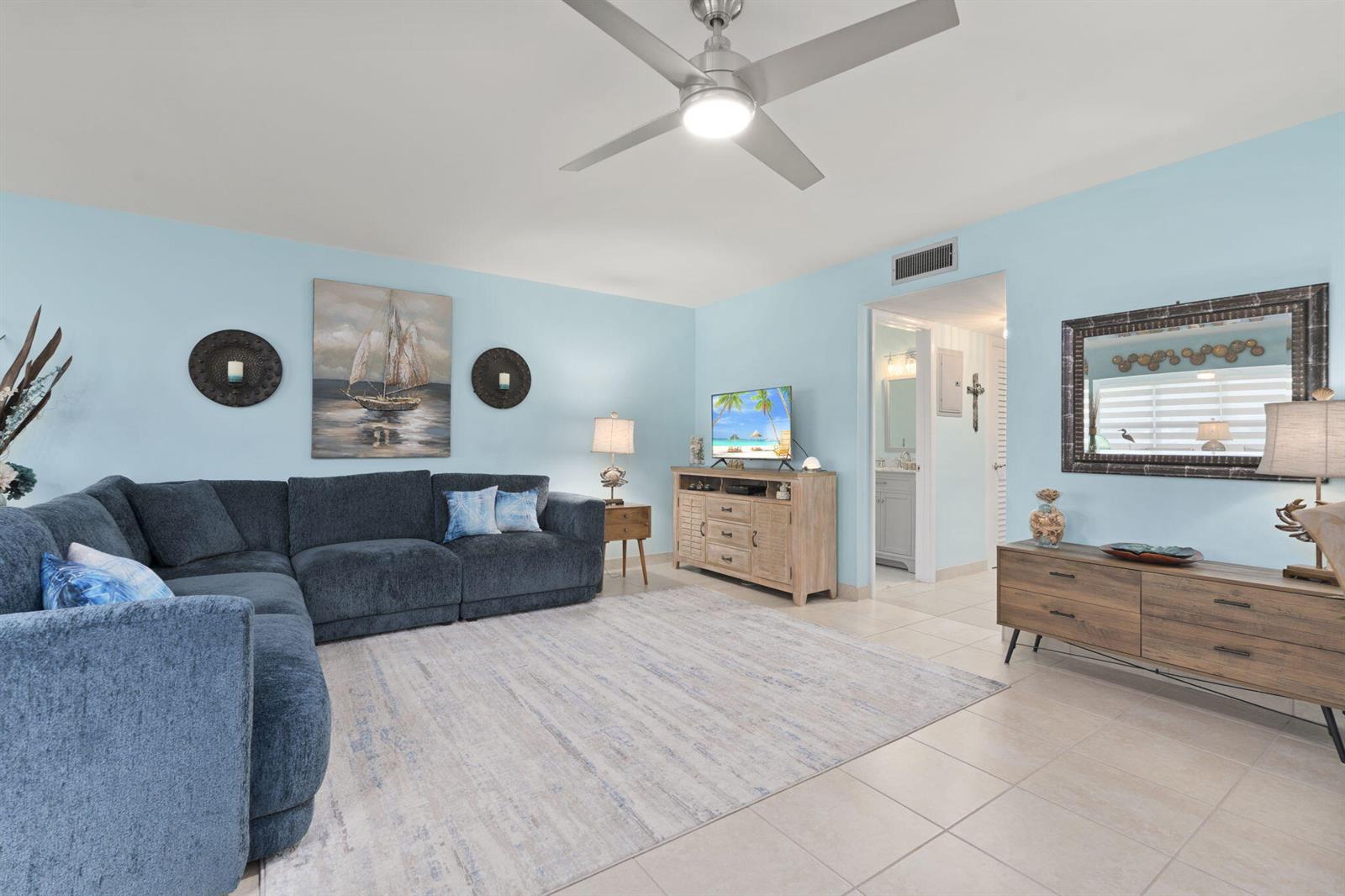 A living room features a blue sectional sofa, a light wood media console, and tile flooring — 1177 S Drive Circle # B, Delray Beach FL 33445, DELRAY BEACH, FL
