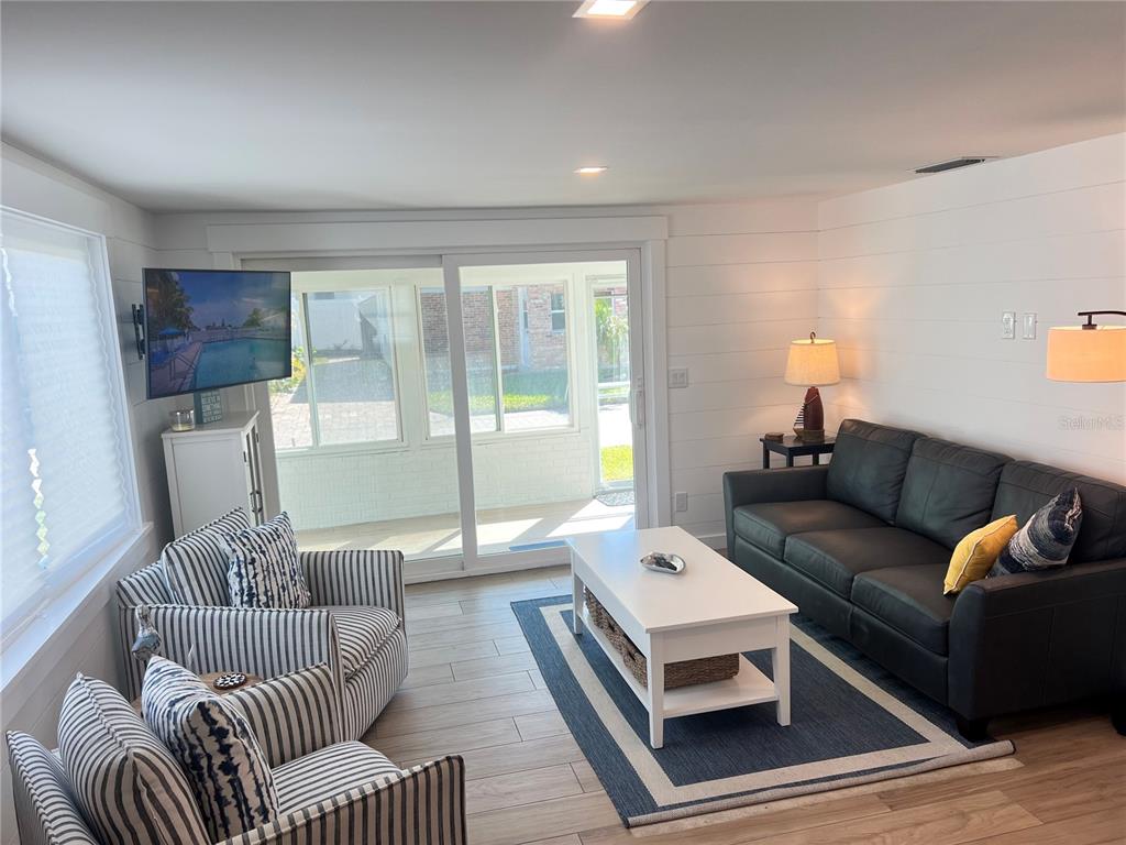 A living room features white shiplap walls, a dark sofa, striped armchairs, and sliding glass doors — 6020 MIDNIGHT PASS ROAD UNIT 54, SARASOTA, FL