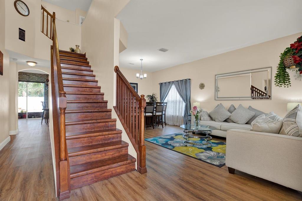 A wooden staircase leads to an upper level next to a living room and dining area — 31405 GLENDALOUGH WAY, WESLEY CHAPEL, FL