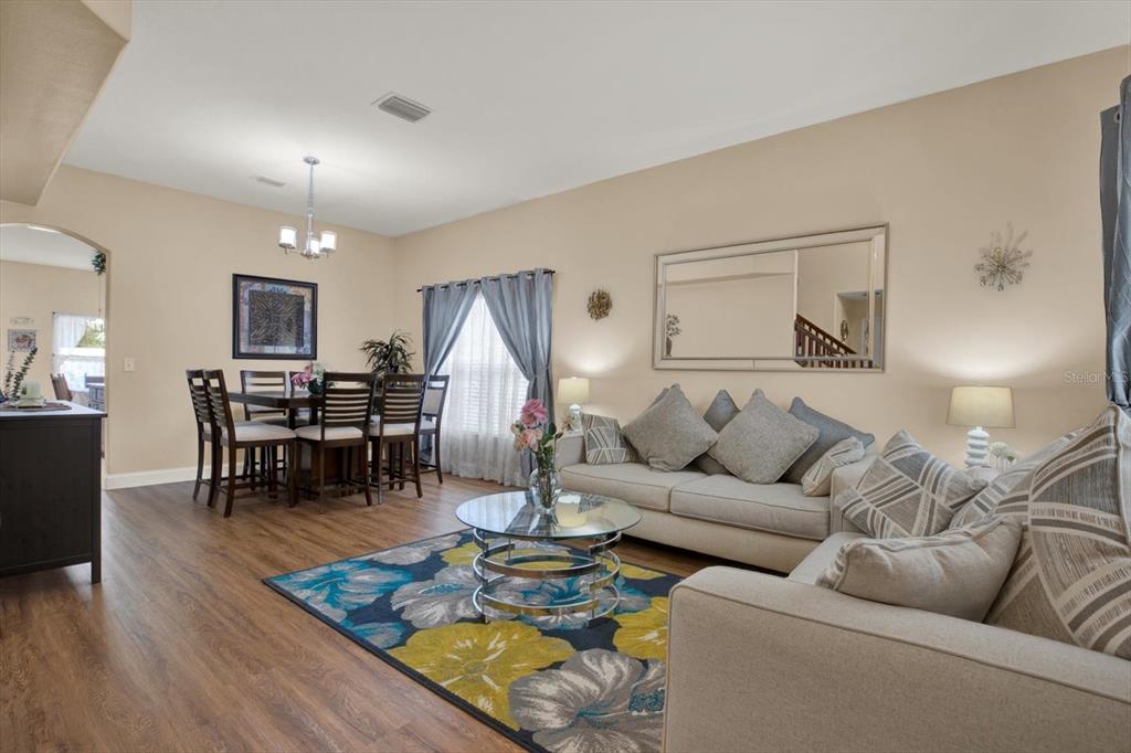 A living room and dining area feature wood-look flooring, a floral rug, and neutral furniture — 31405 GLENDALOUGH WAY, WESLEY CHAPEL, FL