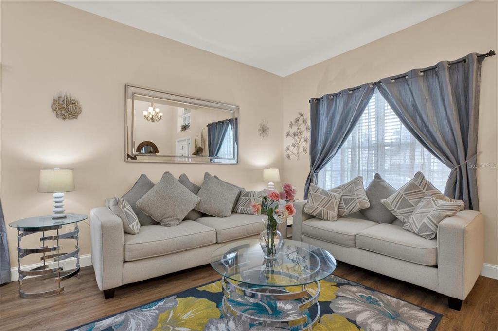 A living room features two light-colored sofas, a glass coffee table, and a large mirror — 31405 GLENDALOUGH WAY, WESLEY CHAPEL, FL