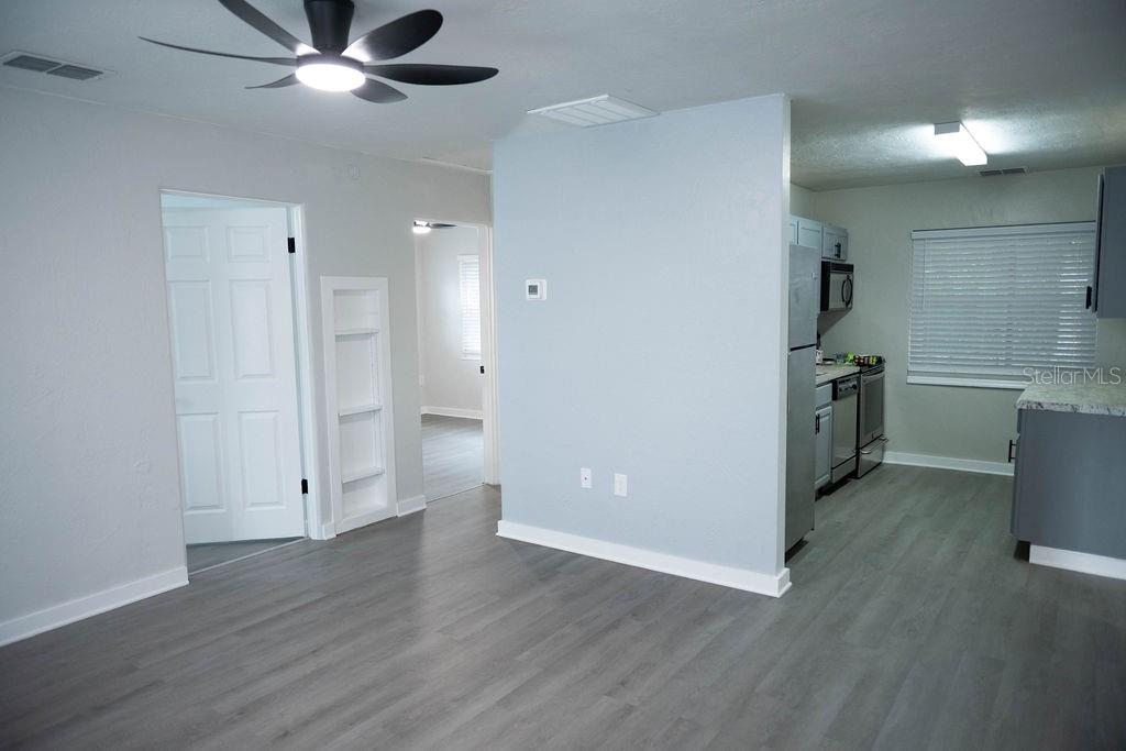 A light-colored room with gray wood-look flooring leads into a kitchen with stainless appliances — 5480 70TH LANE N, ST PETERSBURG, FL
