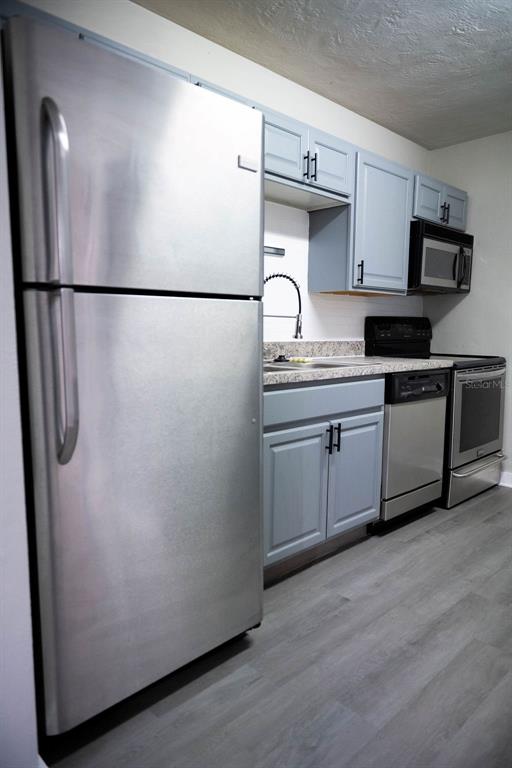 A kitchen features stainless steel appliances, light blue cabinets, and gray wood-look flooring — 5480 70TH LANE N, ST PETERSBURG, FL