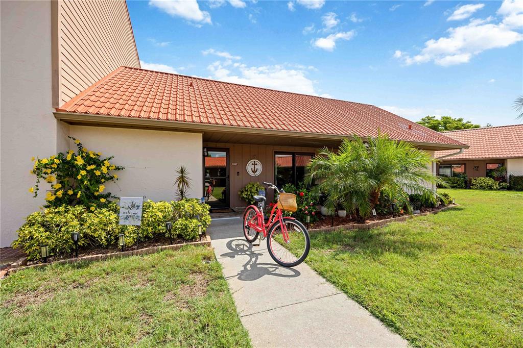 A red bicycle sits on a concrete walkway leading to the entrance of a house — 6507 DRAW LANE UNIT 68, SARASOTA, FL