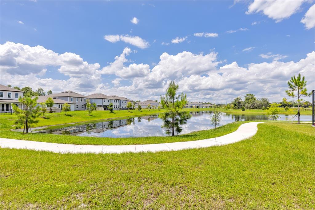 A concrete path curves alongside a retention pond in front of several suburban houses — 2205 BROADBROOK DRIVE, ST CLOUD, FL