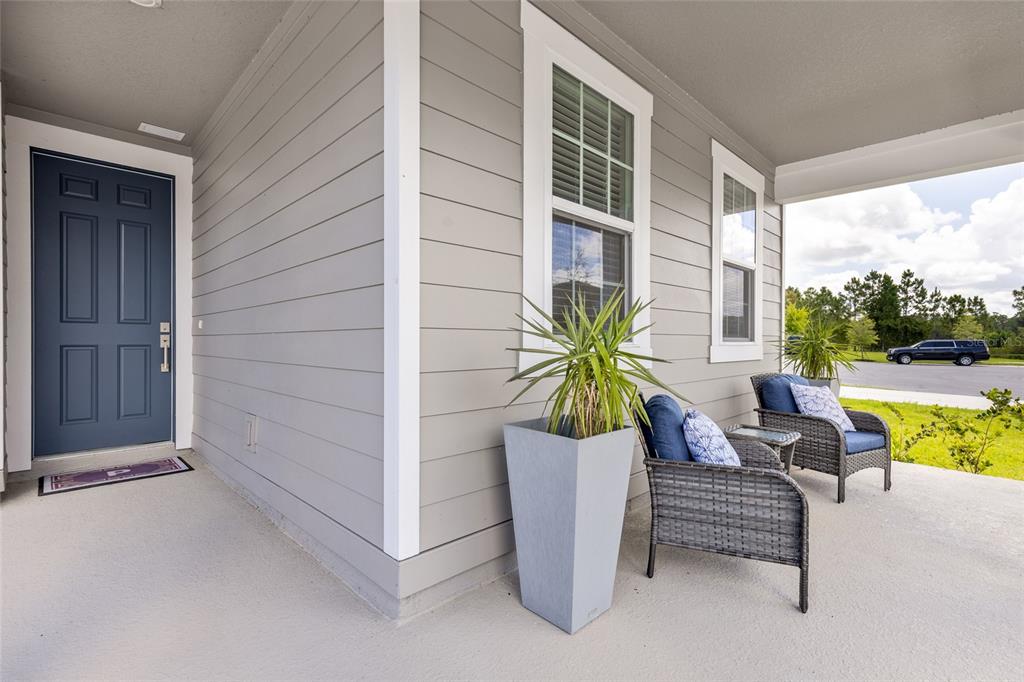 A covered front porch features gray siding, a blue door, and two wicker patio chairs — 2205 BROADBROOK DRIVE, ST CLOUD, FL