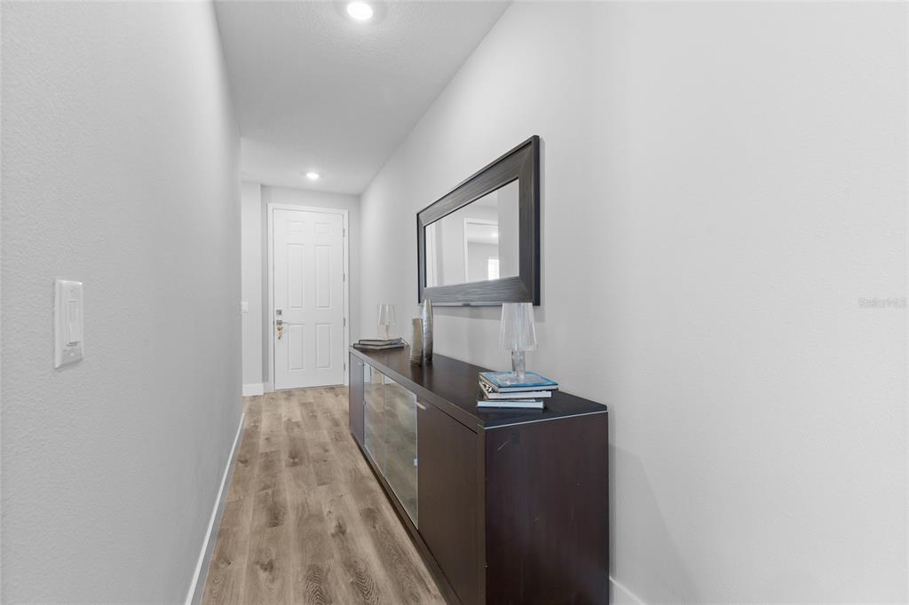 A hallway features light wood-look flooring, a dark console table, and a wall-mounted mirror — 2205 BROADBROOK DRIVE, ST CLOUD, FL