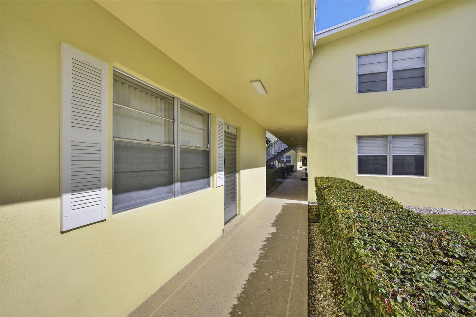 A yellow exterior walkway leads past a doorway and windows alongside a trimmed hedge — 100 Sheffield E, West Palm Beach FL 33417, WEST PALM BEACH, FL