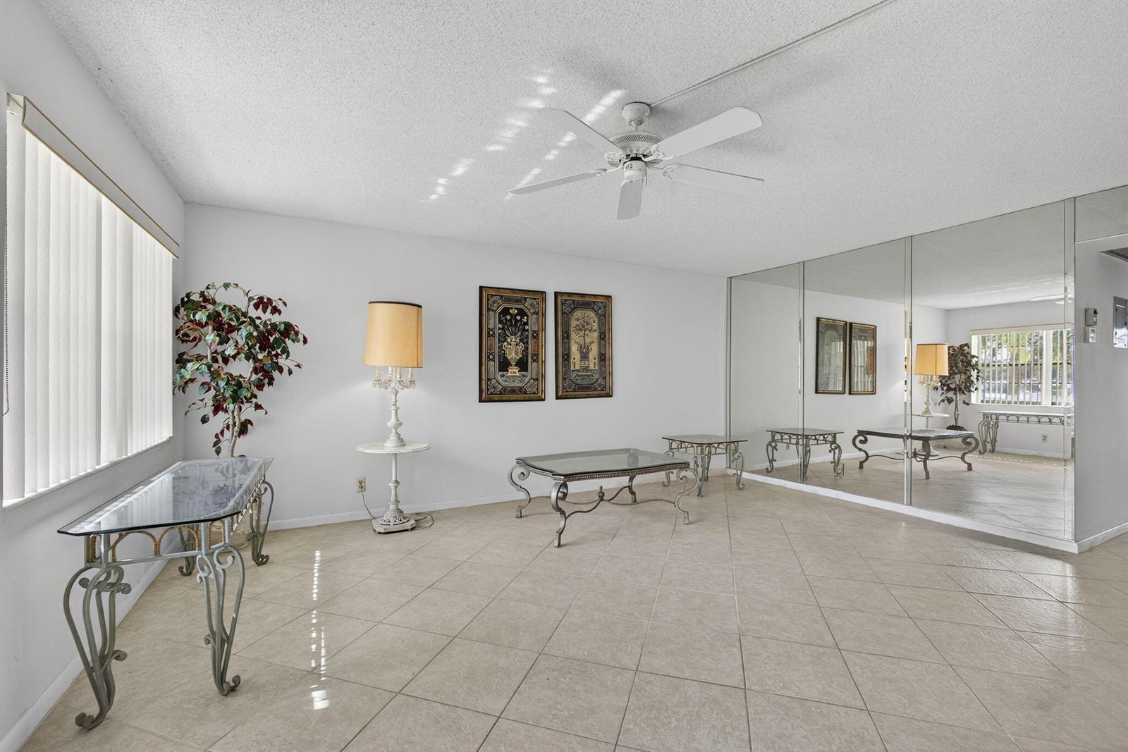 A living room with tile floors, a ceiling fan, mirrored walls, and glass-topped metal furniture — 100 Sheffield E, West Palm Beach FL 33417, WEST PALM BEACH, FL