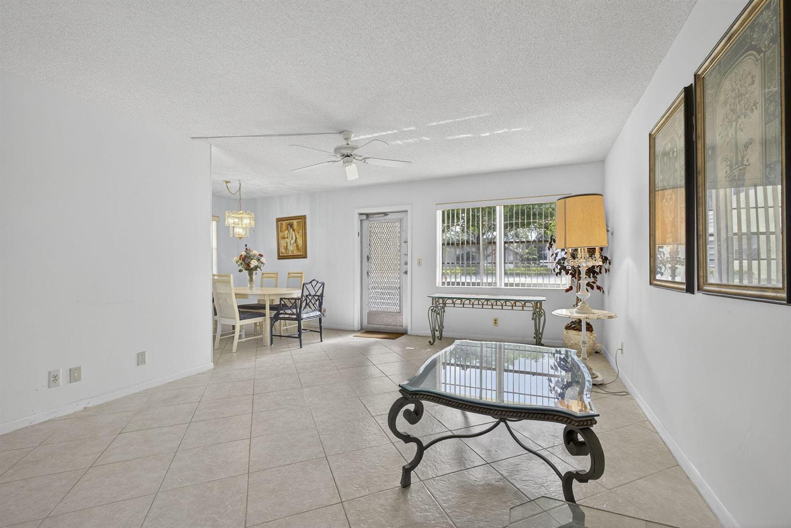 A bright living and dining area features white walls, tile flooring, and a ceiling fan — 100 Sheffield E, West Palm Beach FL 33417, WEST PALM BEACH, FL