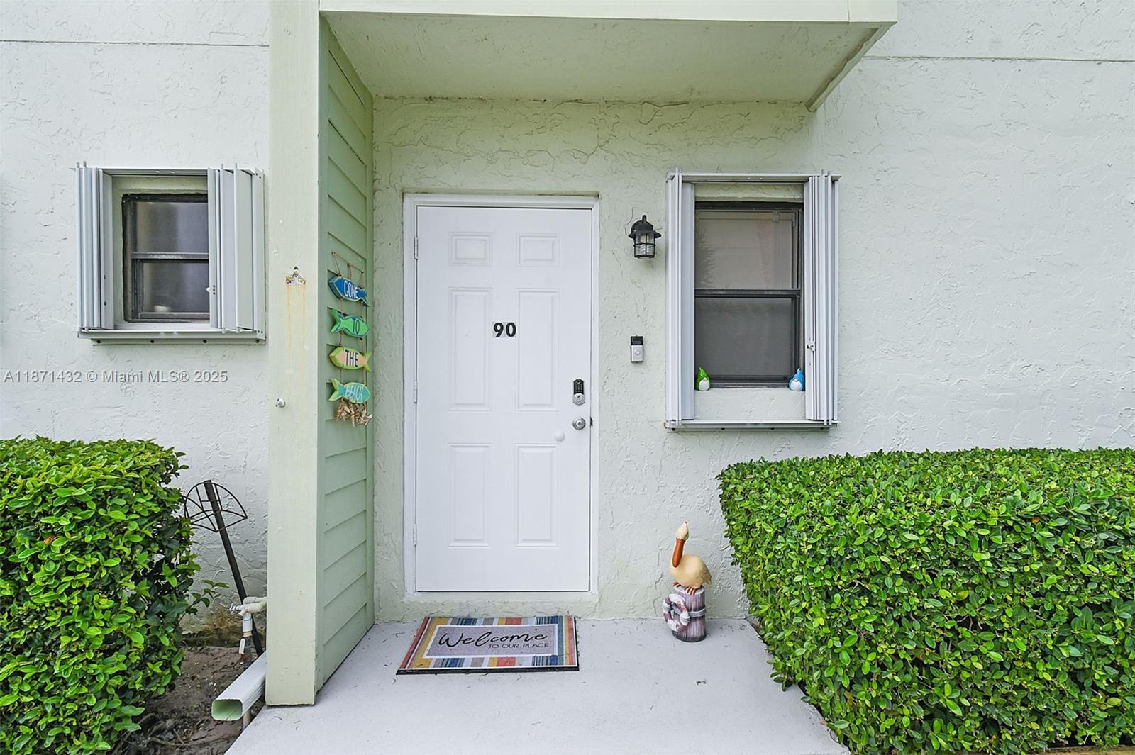 The exterior view shows a white front door labeled 90, flanked by two windows — 9421 S Ocean Dr # 90, Jensen Beach FL 34957, JENSEN BEACH, FL