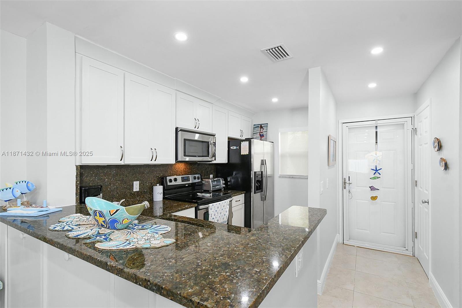 A kitchen features white cabinets, dark granite countertops, and stainless steel appliances — 9421 S Ocean Dr # 90, Jensen Beach FL 34957, JENSEN BEACH, FL