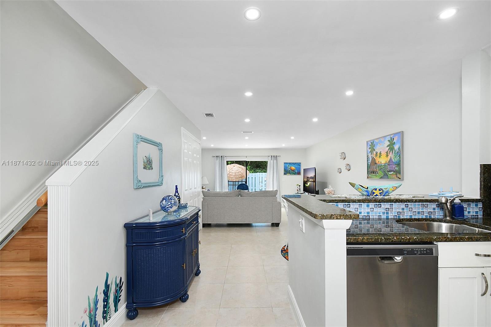 A kitchen with a granite countertop and blue tile backsplash overlooks a living room area — 9421 S Ocean Dr # 90, Jensen Beach FL 34957, JENSEN BEACH, FL