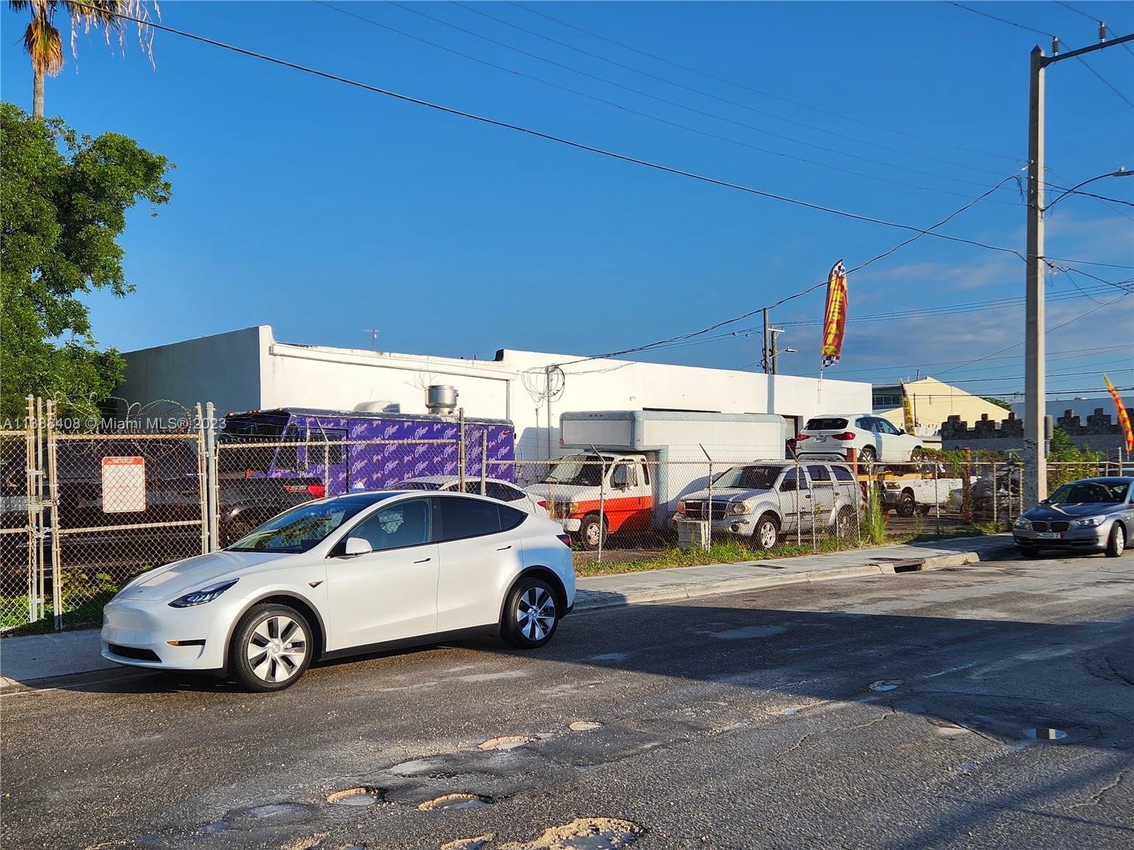 A white Tesla is parked on a street in front of a fenced commercial lot — 60 NW 20th St, Miami FL 33127, MIAMI, FL