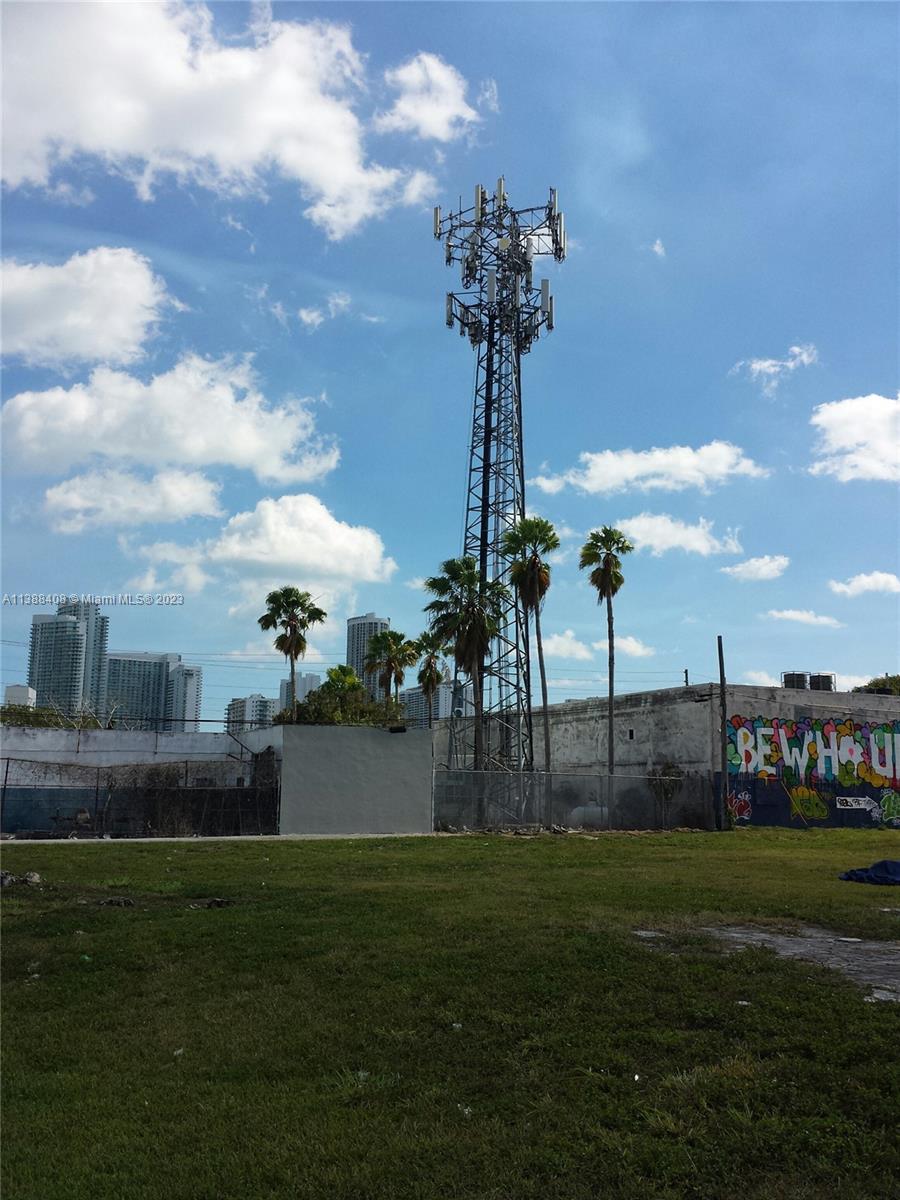 A tall telecommunications tower stands behind a graffiti-covered wall and palm trees in an open lot — 60 NW 20th St, Miami FL 33127, MIAMI, FL